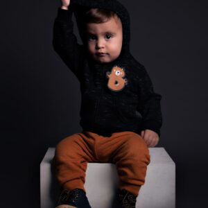 Charming portrait of a toddler wearing a stylish hoodie, posing indoors against a dark background.