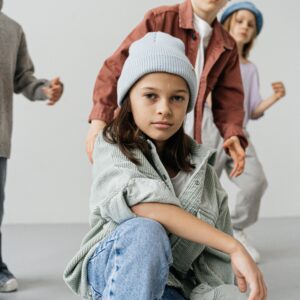 Four children in fashionable jackets and caps posing creatively against a white background.